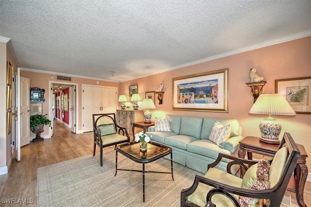 living room featuring a textured ceiling, ornamental molding, wood finished floors, and visible vents