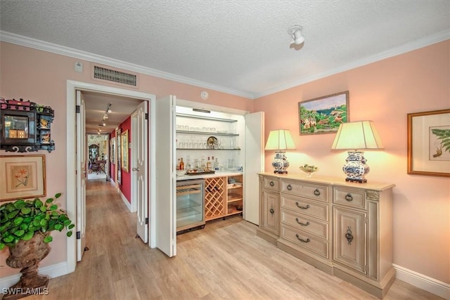 corridor with beverage cooler, a textured ceiling, light wood-type flooring, and visible vents