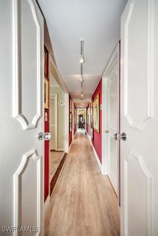 hallway featuring rail lighting, light wood-style flooring, and baseboards