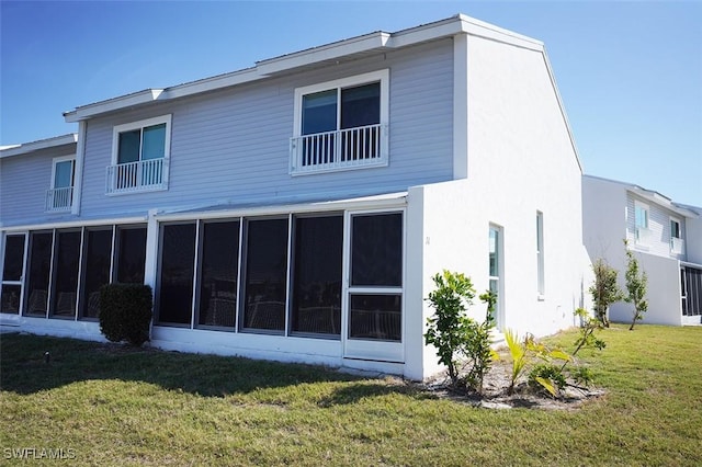 back of property with a lawn, a sunroom, and stucco siding