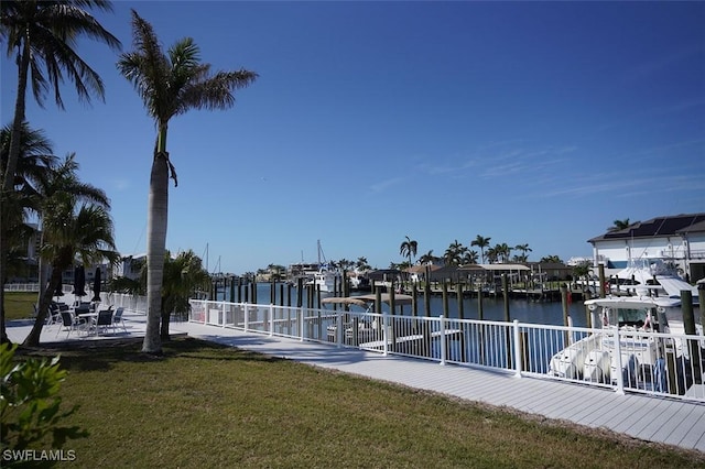 view of dock featuring a water view, fence, boat lift, and a lawn