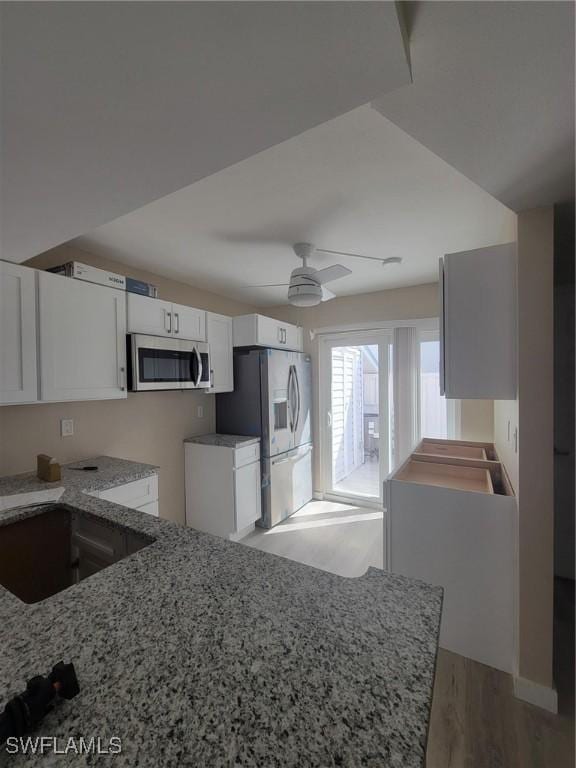 kitchen featuring light wood finished floors, white cabinets, a ceiling fan, light stone countertops, and stainless steel appliances