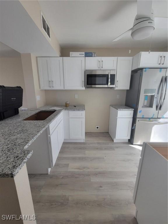 kitchen featuring a sink, white cabinetry, visible vents, appliances with stainless steel finishes, and light stone countertops