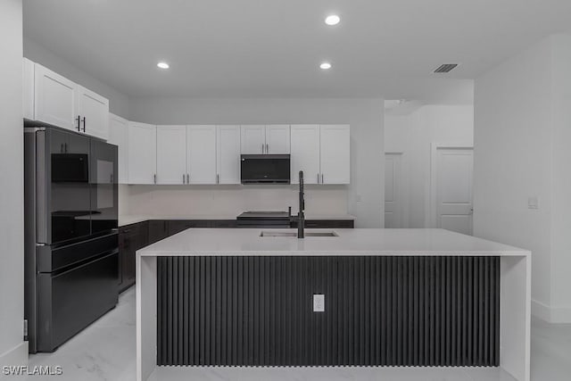 kitchen with a center island with sink, light countertops, visible vents, freestanding refrigerator, and white cabinetry