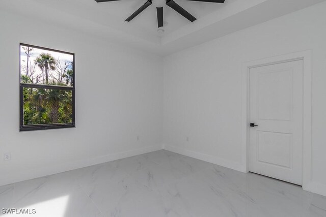 empty room featuring marble finish floor, ceiling fan, baseboards, and a tray ceiling