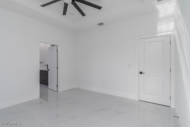 spare room with a tray ceiling, marble finish floor, visible vents, ceiling fan, and baseboards