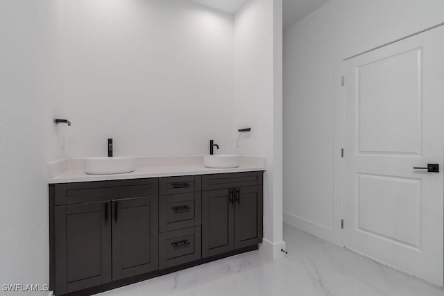 full bath featuring marble finish floor, a sink, baseboards, and double vanity