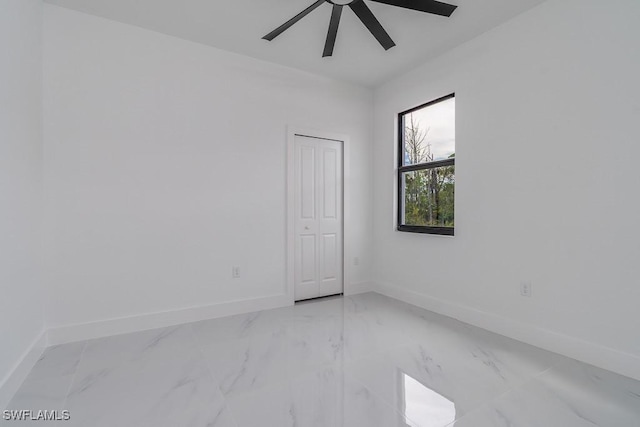 empty room featuring ceiling fan, marble finish floor, and baseboards