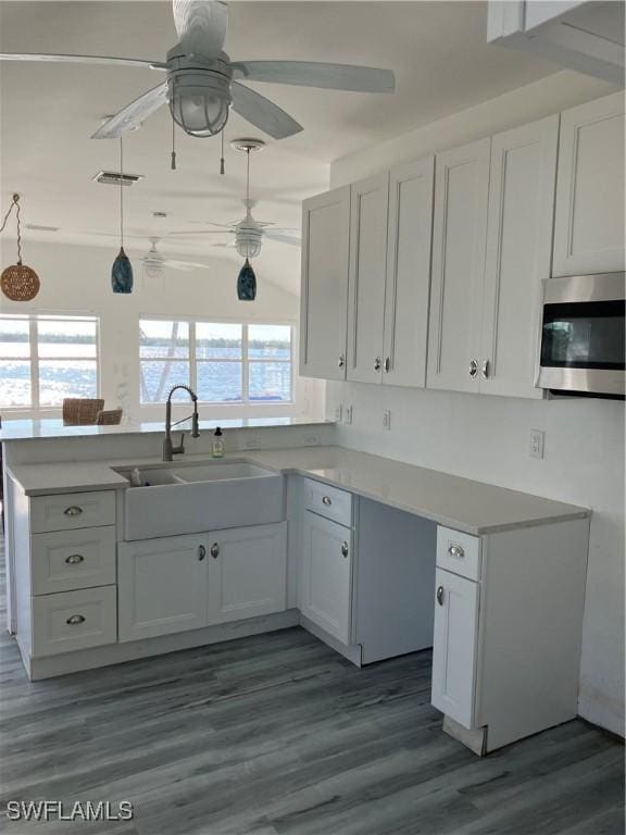 kitchen featuring light countertops, stainless steel microwave, a sink, wood finished floors, and a peninsula