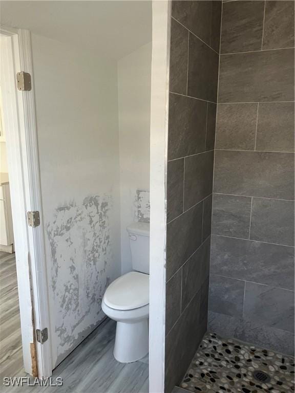 bathroom with toilet, a tile shower, and wood finished floors