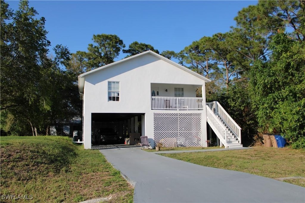 view of front facade featuring driveway, stairway, covered porch, a front lawn, and stucco siding