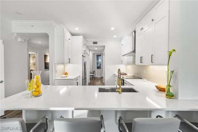 kitchen with white cabinets, wall chimney range hood, tasteful backsplash, stainless steel fridge, and crown molding