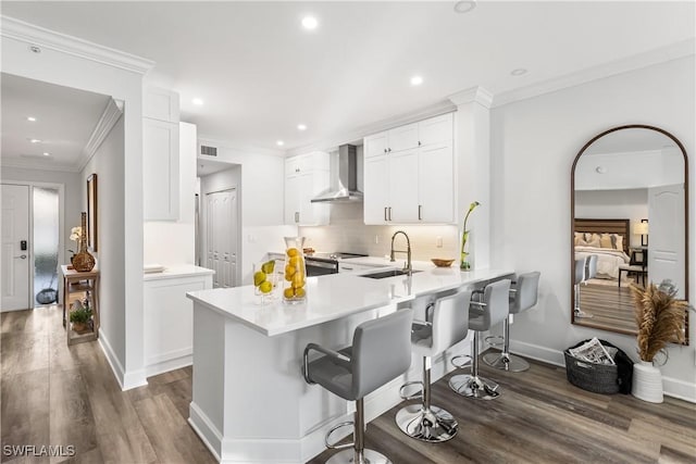 kitchen featuring a breakfast bar area, tasteful backsplash, a sink, wall chimney range hood, and a peninsula