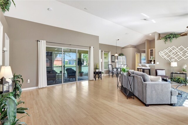 living area featuring high vaulted ceiling, light wood-type flooring, visible vents, and baseboards