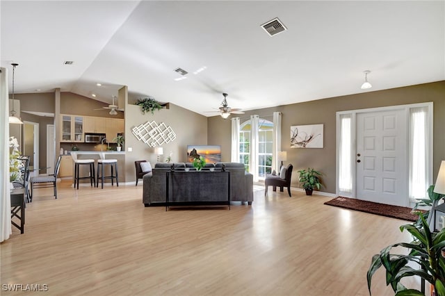 living area with lofted ceiling, light wood finished floors, baseboards, and visible vents