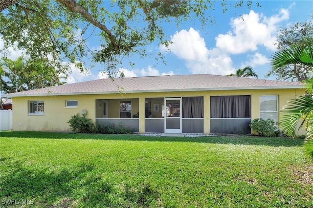 rear view of property featuring a sunroom, a lawn, and stucco siding