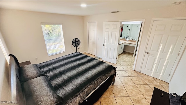 bedroom featuring ensuite bath, light tile patterned floors, and visible vents