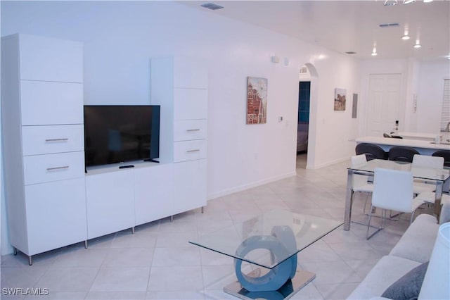 living area featuring light tile patterned floors, baseboards, visible vents, and arched walkways