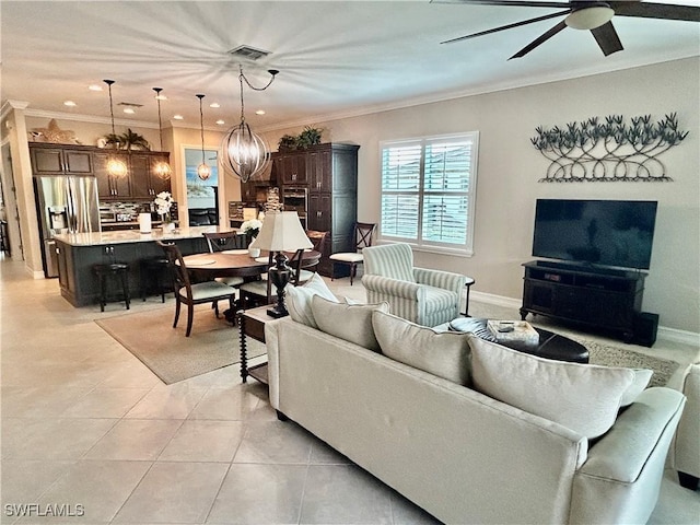 living room with light tile patterned floors, ceiling fan with notable chandelier, visible vents, baseboards, and ornamental molding