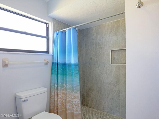 full bath featuring toilet, a textured ceiling, and tiled shower