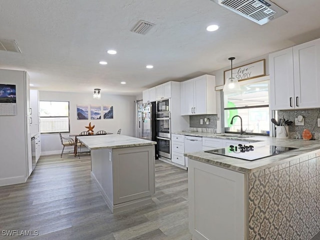 kitchen with a kitchen island, visible vents, light wood-type flooring, backsplash, and black appliances