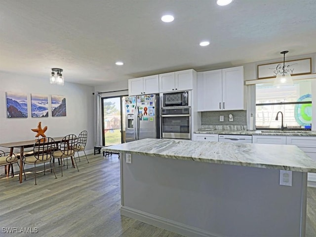 kitchen featuring stainless steel appliances, a sink, white cabinets, light wood-style floors, and backsplash