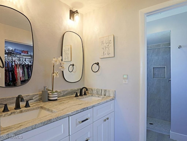 full bath with double vanity, a tile shower, a sink, and a walk in closet