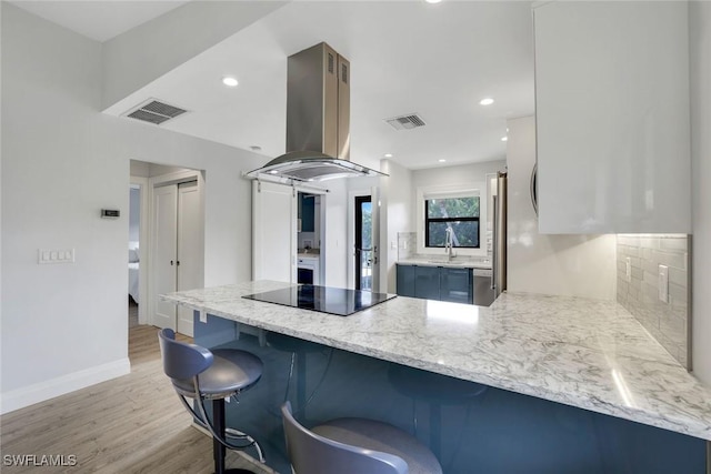 kitchen featuring visible vents, island exhaust hood, a peninsula, and black electric stovetop