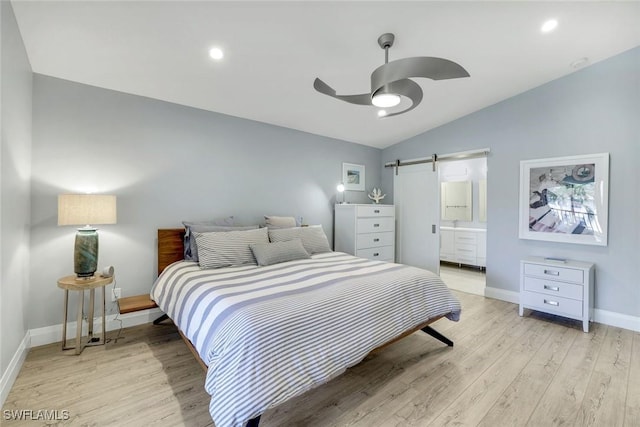 bedroom with light wood finished floors, lofted ceiling, a barn door, ensuite bath, and baseboards