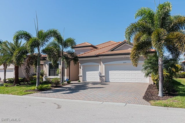 mediterranean / spanish-style home featuring a tiled roof, decorative driveway, an attached garage, and stucco siding