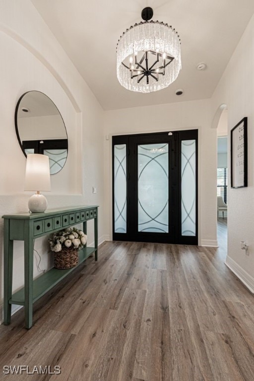 entryway with baseboards, a notable chandelier, arched walkways, and wood finished floors