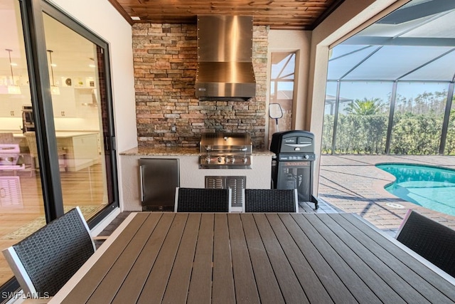 deck featuring area for grilling, an outdoor kitchen, a patio area, glass enclosure, and an outdoor pool