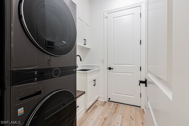 clothes washing area with light wood finished floors, stacked washer / dryer, a sink, and cabinet space