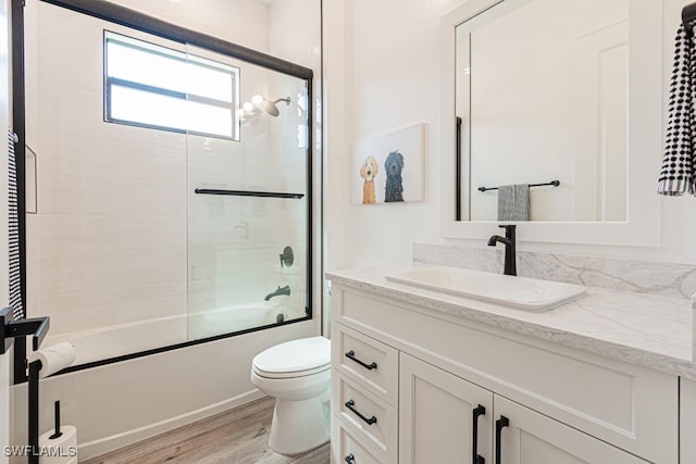 bathroom with toilet, shower / bath combination with glass door, wood finished floors, and vanity