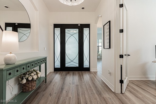 foyer entrance featuring arched walkways, baseboards, and wood finished floors