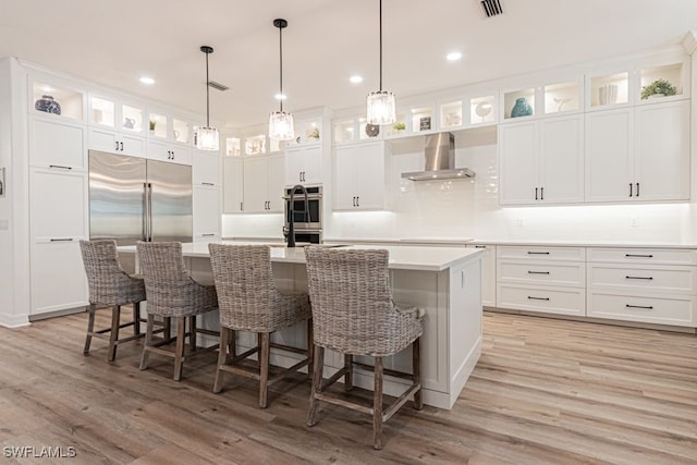 kitchen featuring stainless steel appliances, wall chimney range hood, a large island with sink, and light wood-style flooring