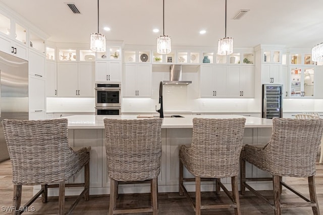 kitchen featuring stainless steel appliances, wall chimney range hood, a spacious island, and visible vents