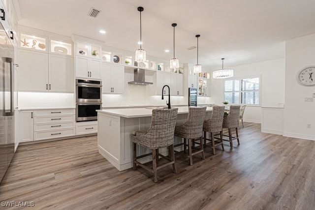 kitchen featuring stainless steel double oven, light wood-style flooring, visible vents, light countertops, and wall chimney exhaust hood