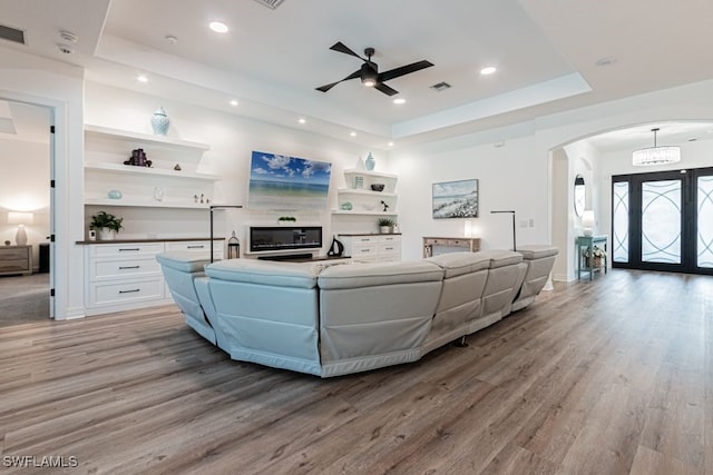 living area with light wood-style flooring, arched walkways, a raised ceiling, and recessed lighting