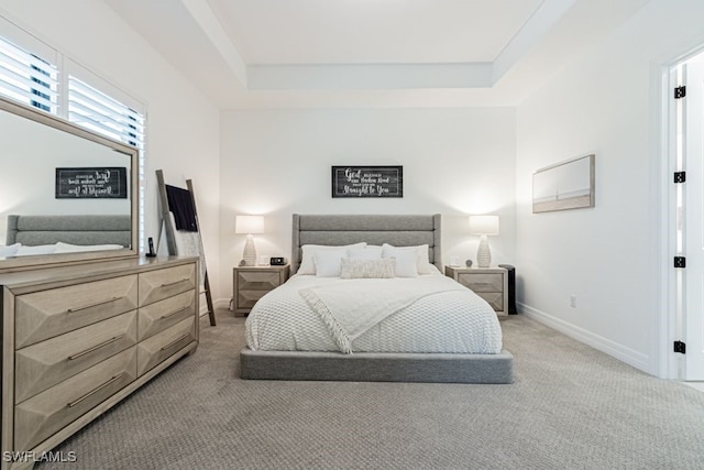 bedroom featuring light carpet, a tray ceiling, and baseboards