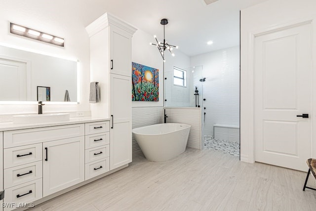 bathroom featuring wood finished floors, an inviting chandelier, a freestanding bath, vanity, and a walk in shower