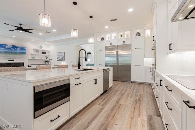 kitchen featuring light wood finished floors, white cabinets, built in appliances, extractor fan, and a sink