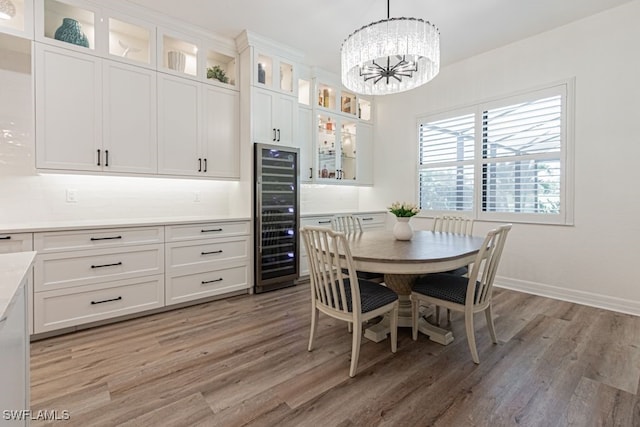 dining space with light wood-style flooring, wine cooler, a chandelier, and baseboards