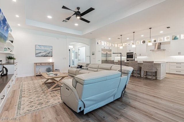 living room featuring arched walkways, a tray ceiling, light wood finished floors, recessed lighting, and visible vents