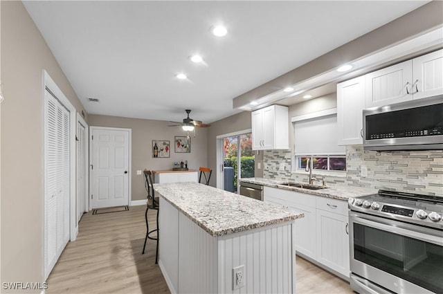 kitchen featuring stainless steel appliances, a sink, white cabinets, backsplash, and a center island