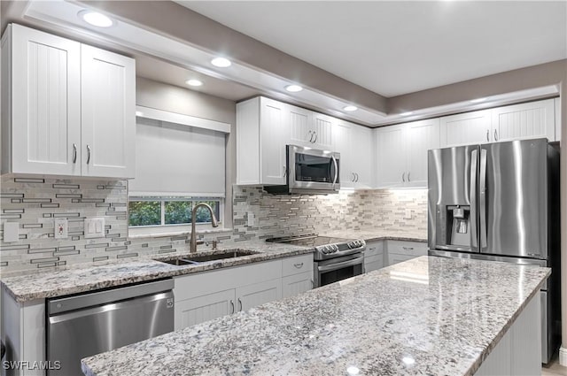 kitchen with stainless steel appliances, backsplash, white cabinetry, a sink, and light stone countertops