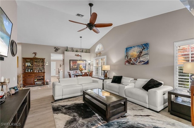 living room with ceiling fan, high vaulted ceiling, light wood finished floors, and visible vents