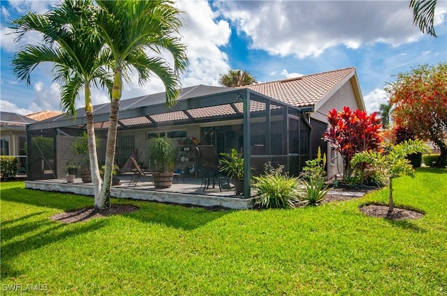 back of property featuring a yard, a tile roof, glass enclosure, and a patio