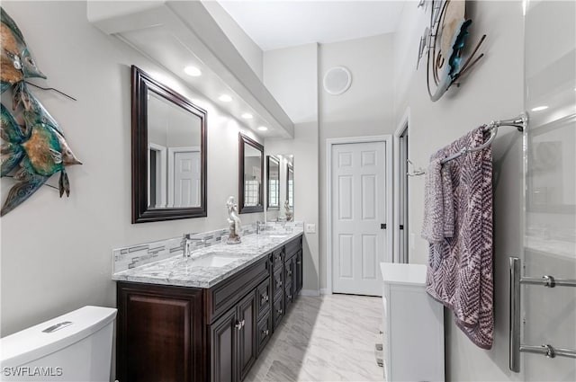 bathroom featuring marble finish floor, double vanity, a sink, and toilet