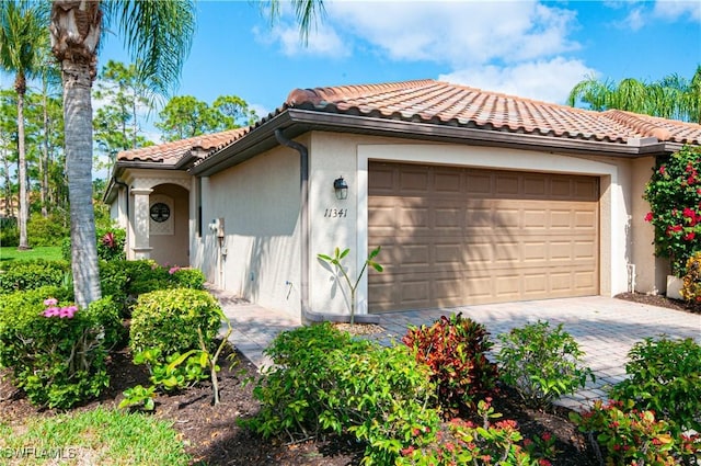 exterior space featuring an attached garage, stucco siding, decorative driveway, and a tiled roof